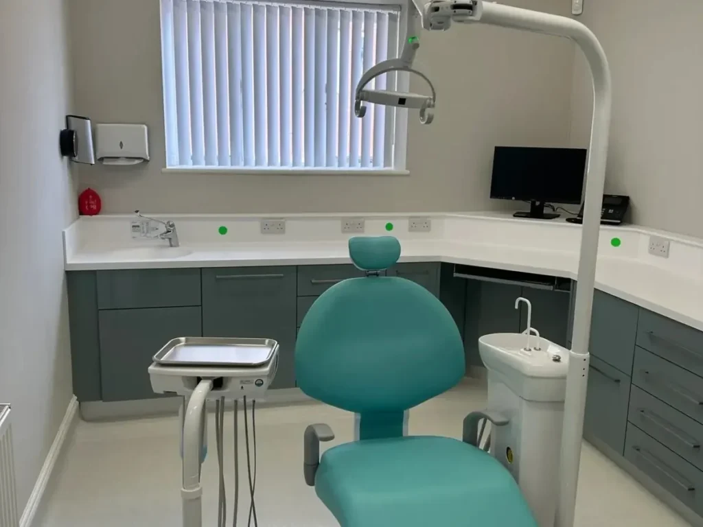 Upstairs dental hygiene surgery at Rectory Dental Clinic with a turquoise dental chair, overhead examination light, modern cabinetry, and hygiene treatment equipment.